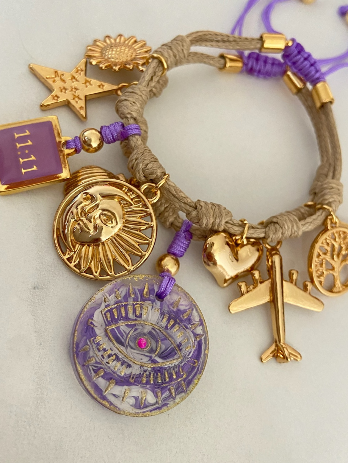 Pulsera marrón claro con ojo de resina lila y dijes dorados – Ajustable