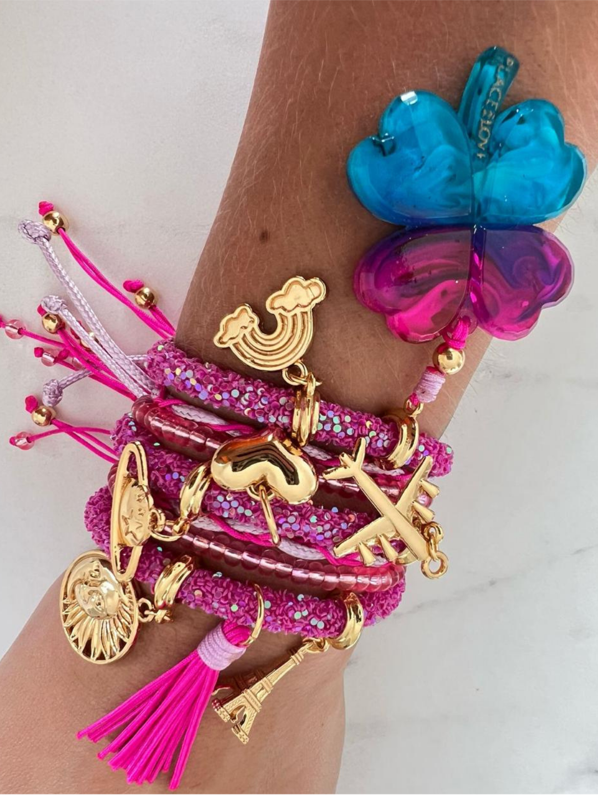 Rosafarbenes Strassarmband mit rosa-lila-blauem Kleeblatt-Anhänger und goldenen Glücksbringern.