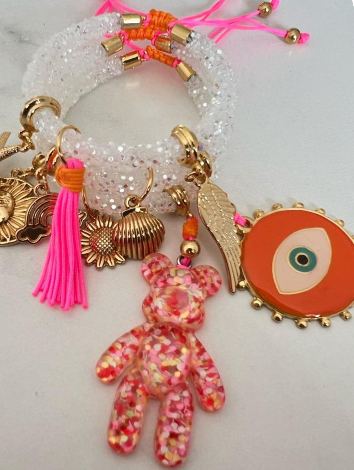 Weißes Strassarmband mit orangefarbenem bösen Blick, orange-weißem Bären und goldenen Glücksbringern