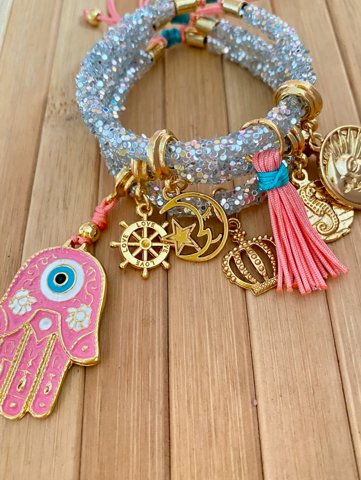 Grey rhinestone bracelet with pink Hamsa hand and coral tassel worn on wrist, showing gold charm detail – IsabellaByShop