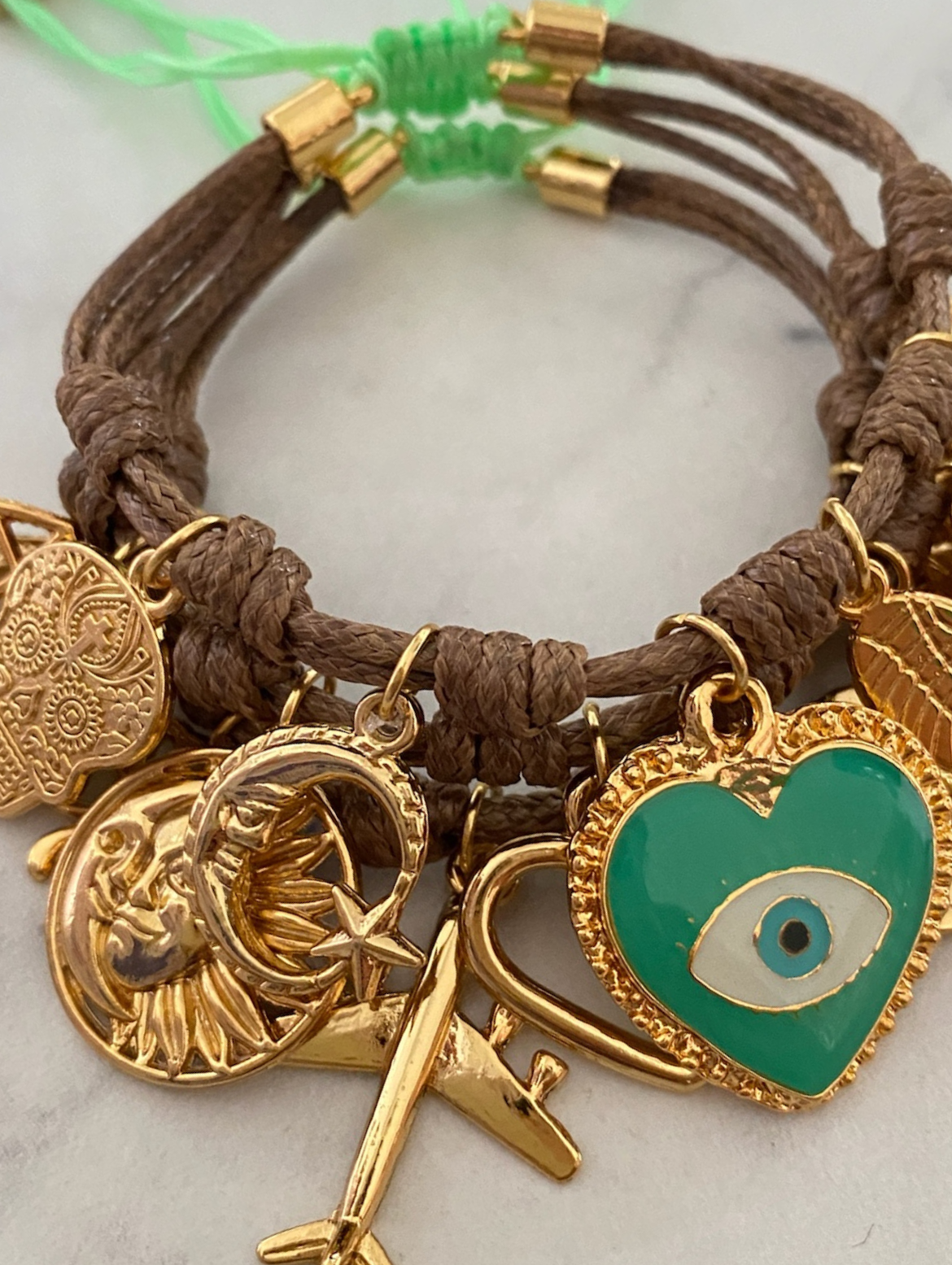 Braunes Armband von Vibora mit grünem Herz und goldenen Glücksbringern.