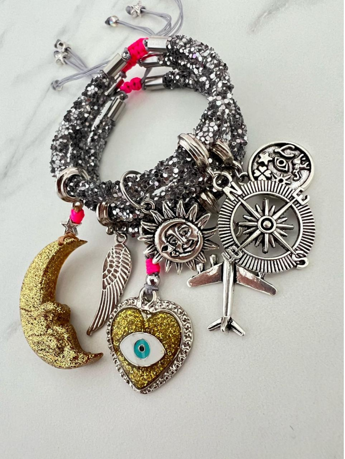 Silver sequin rhinestone cord charm bracelets with pink thread accents, featuring silver and gold-tone charms including a glitter moon, angel wing, compass, airplane, sun face, zodiac coin, and gold heart with evil eye.