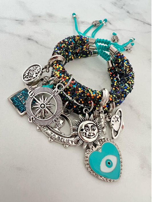 Dark green rainbow rhinestone cord charm bracelets with turquoise thread, featuring silver and enamel charms including a sun face, compass, turquoise evil eye heart, planet, 'I Want to Believe' banner, and 11:11 glitter tag.