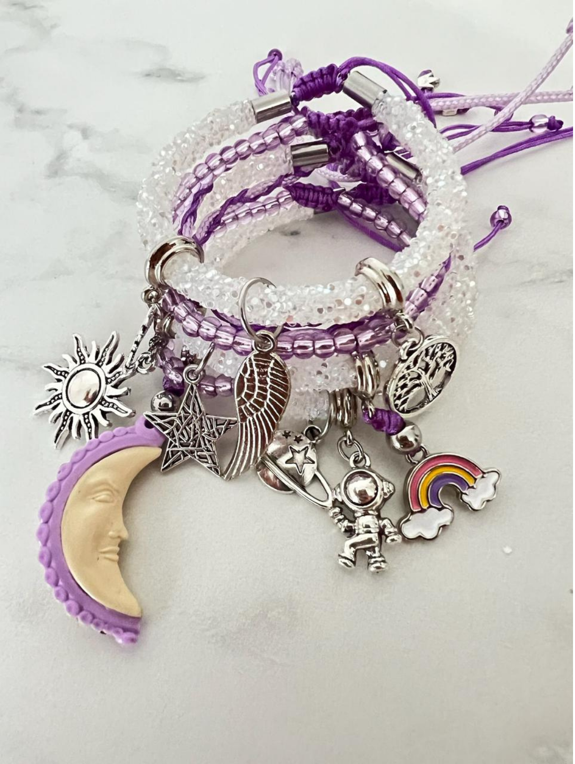 Handmade bracelet set in lilac and light pink tones with beaded cords and silver charms including a moon, sun angel, rainbow and wing in a dreamy boho style. 