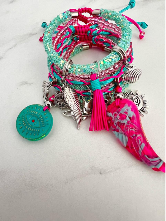 Handmade stack of green and fucsia bracelets with braided cords, silver charms including a wing and Maya evil eye, crystal beads and fucsia floral fabric tassel in a vibrant boho style. 